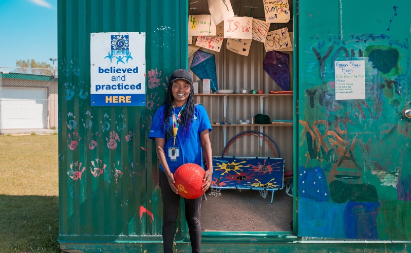 Green Shack worker standing in front of shed holding basketball