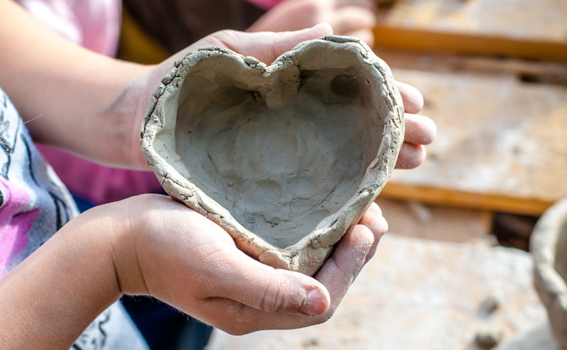 A child's hands holding a heart-shaped bowl made of clay.