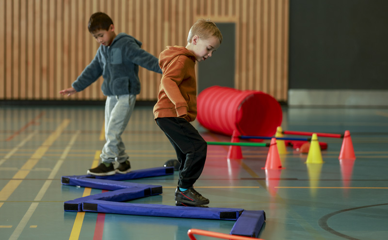 Two boys playing on a balancing beam mat in a gymnasium.