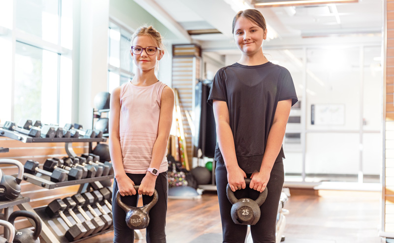 Two young girls holding kettlebells in a fitness centre.