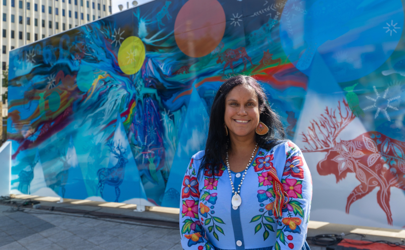 Artist standing in front of mural on back of Edmonton sign